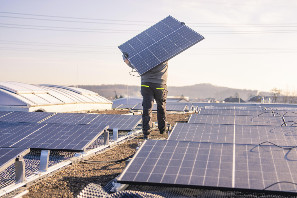 Ein Arbeiter steht mit einem Solarpaneel auf einem Dach